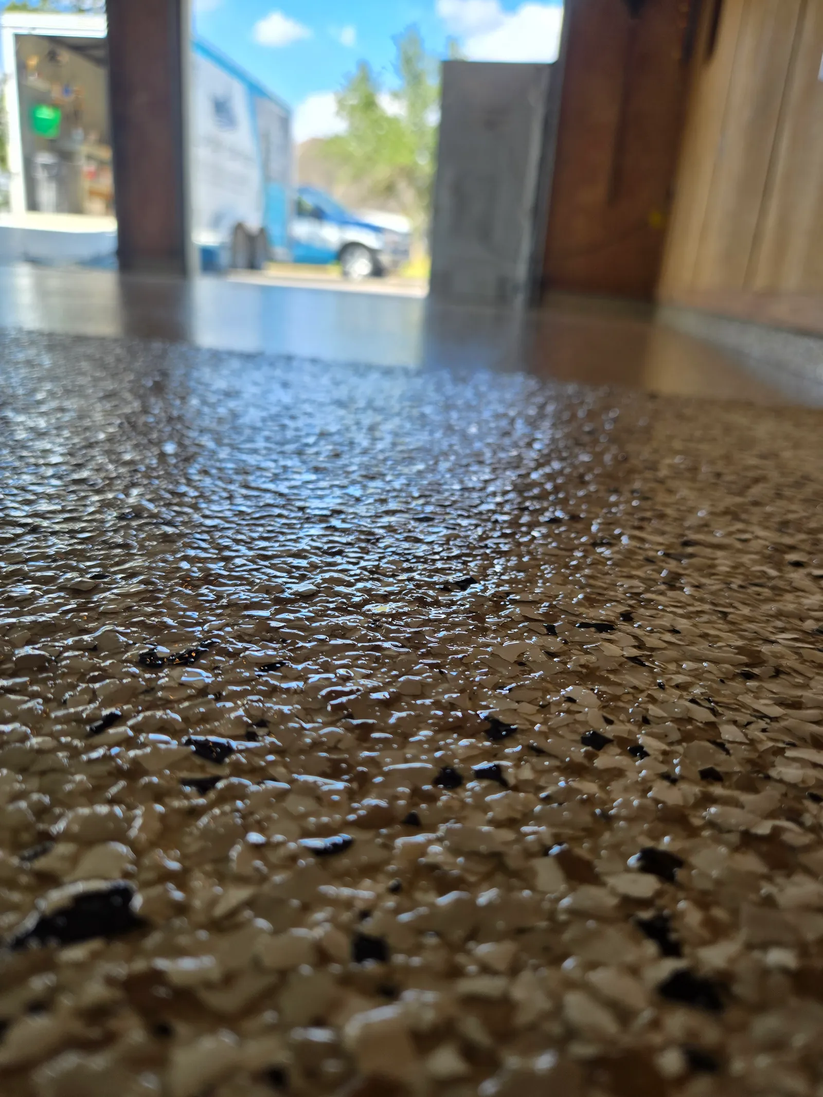 Low-angle close-up of a tan and black flake epoxy garage floor finished to a high gloss