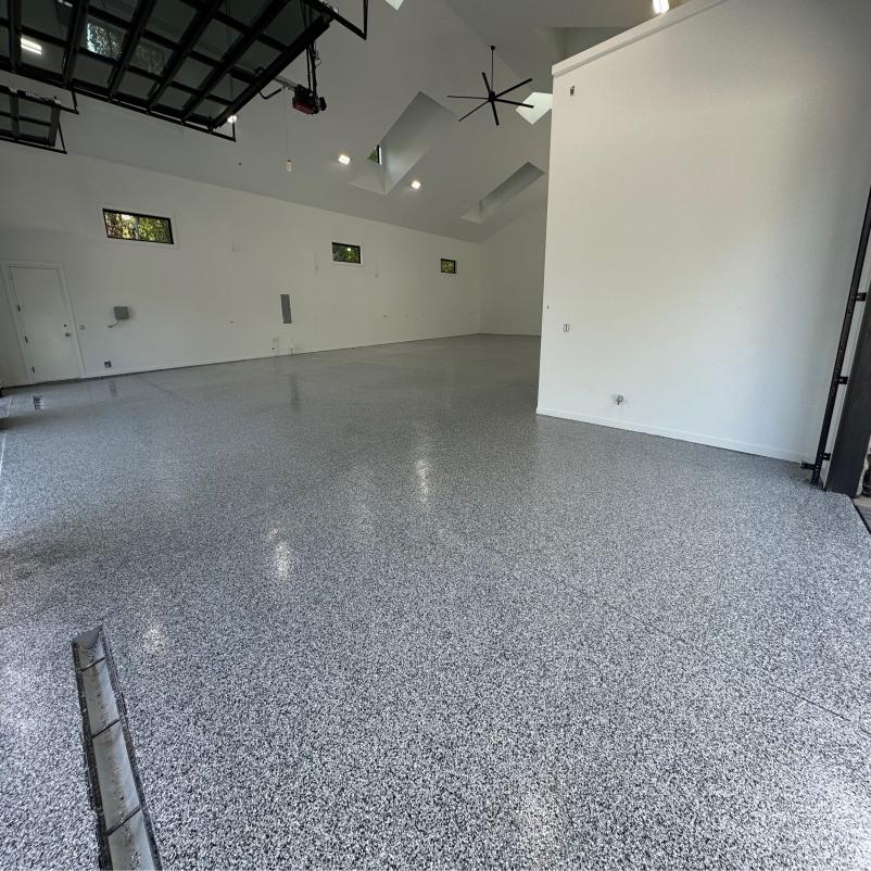 Spacious, empty garage with polished speckled floors, white walls, and black ceilings. Natural light filters through high windows, illuminating the modern space.