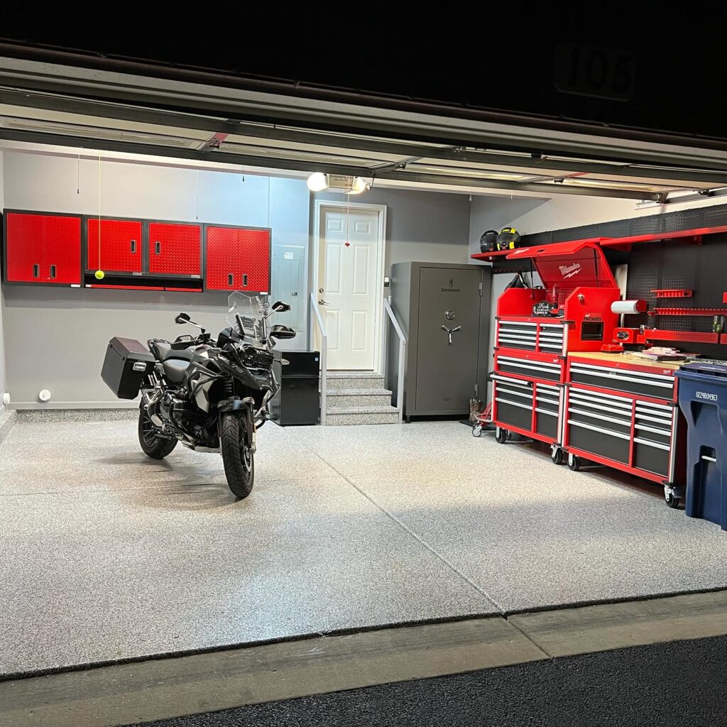 Motorcycle parked in a tidy garage with red tool cabinets, drawers, and a secure safe. Modern, well-organized space with gray flooring.