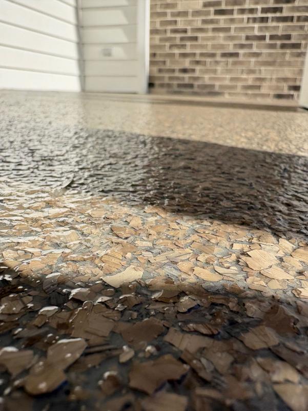 Textured surface with beige and brown tones leads to a brick wall. Sunlight creates shadows, enhancing the contrast and texture.