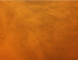 The image displays a textured orange surface with subtle variations and patterns, resembling a painted or plastered wall, with no discernible landmarks.